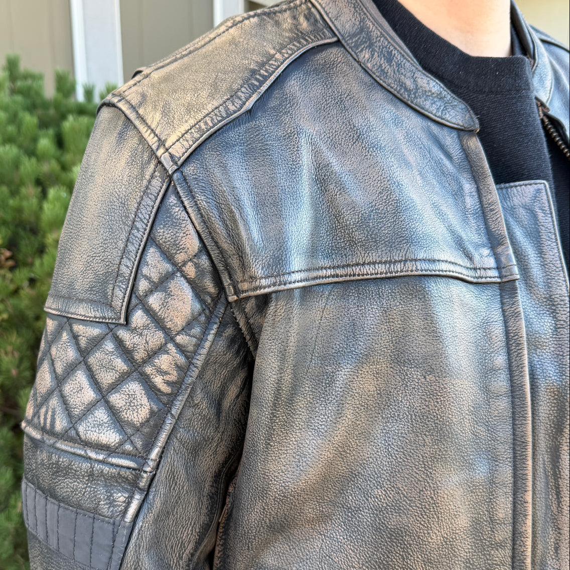 A man wearing a distressed brown leather motorcycle jacket with geometric diamond-stitch detailing on the shoulders