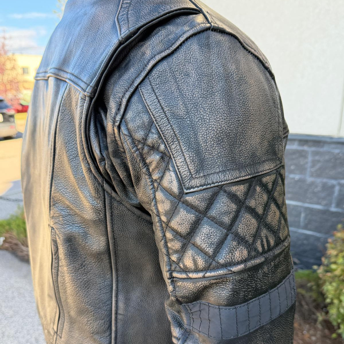 A man wearing a distressed brown leather motorcycle jacket with geometric diamond-stitch detailing on the shoulders