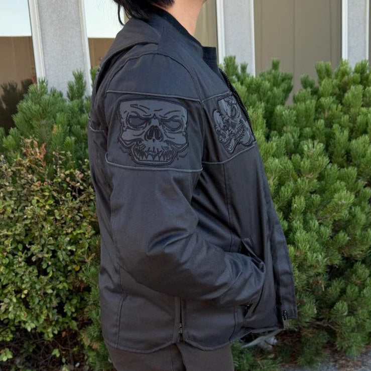 A man wearing a black bomber motorcycle jacket with intricate black embroidery across the chest