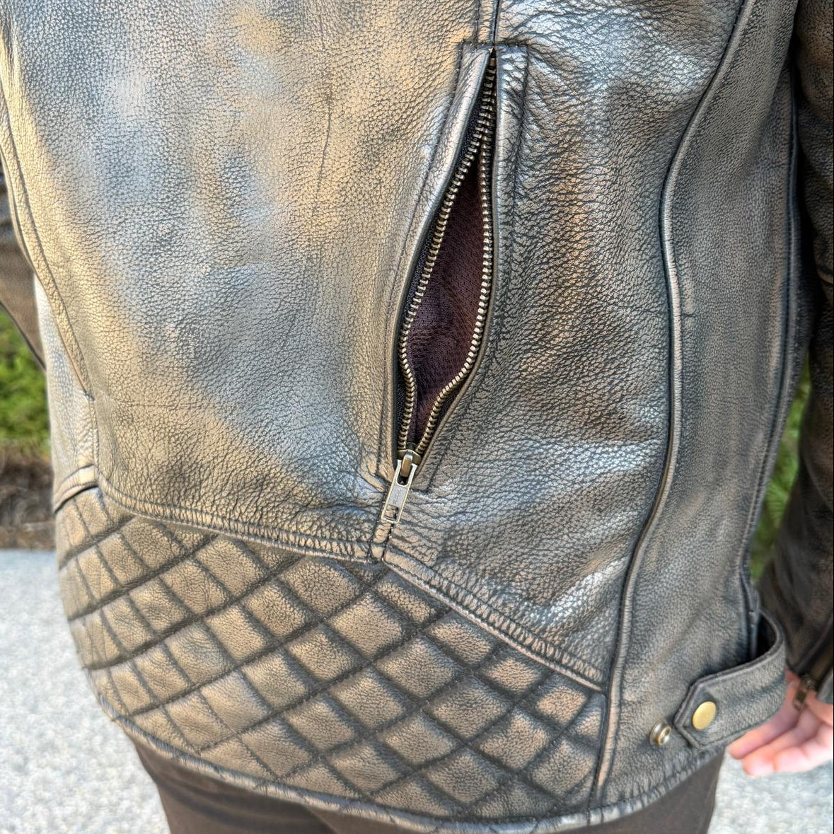 A man wearing a distressed brown leather motorcycle jacket with geometric diamond-stitch detailing on the shoulders