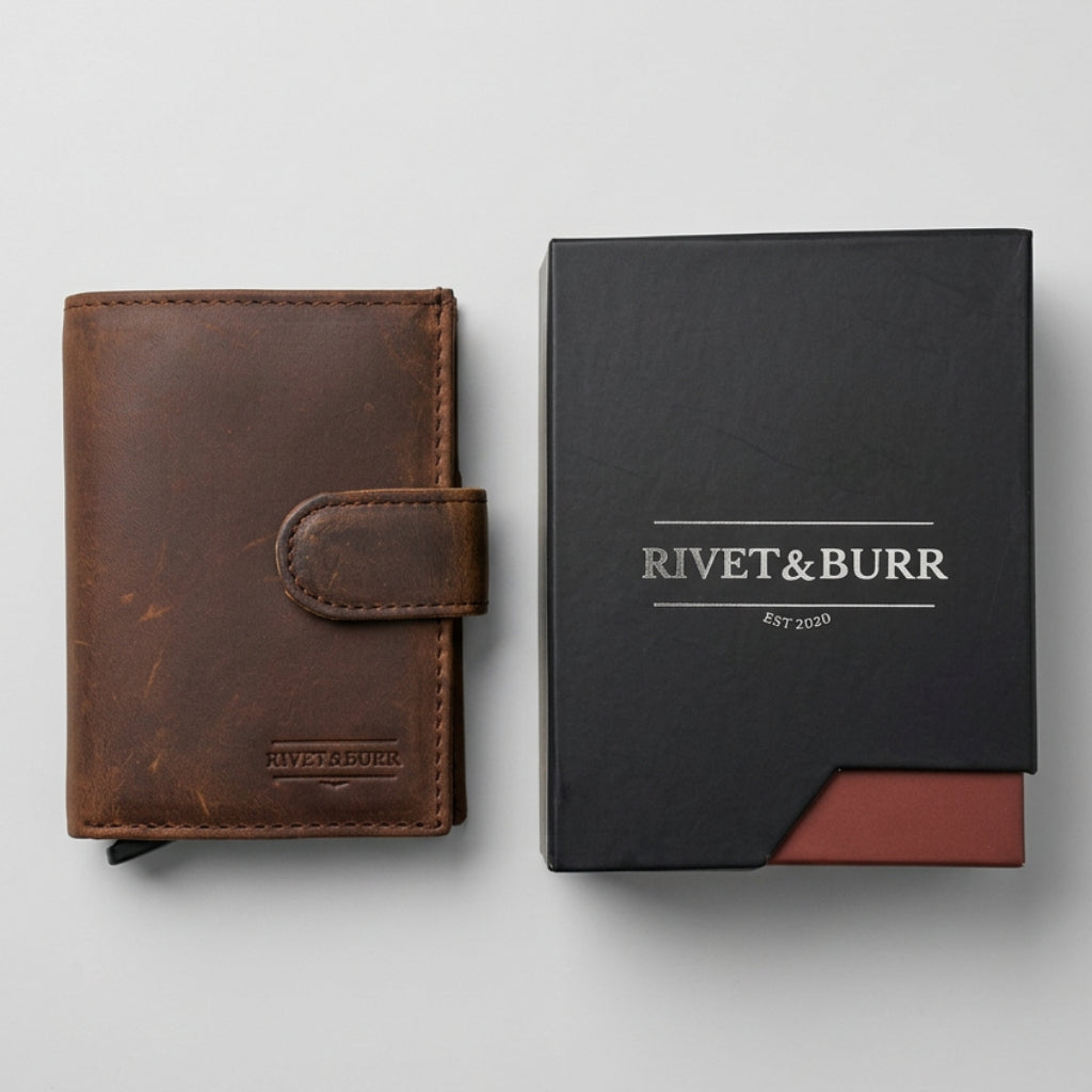 A brown leather bifold wallet next to its black Rivet & Burr branded box