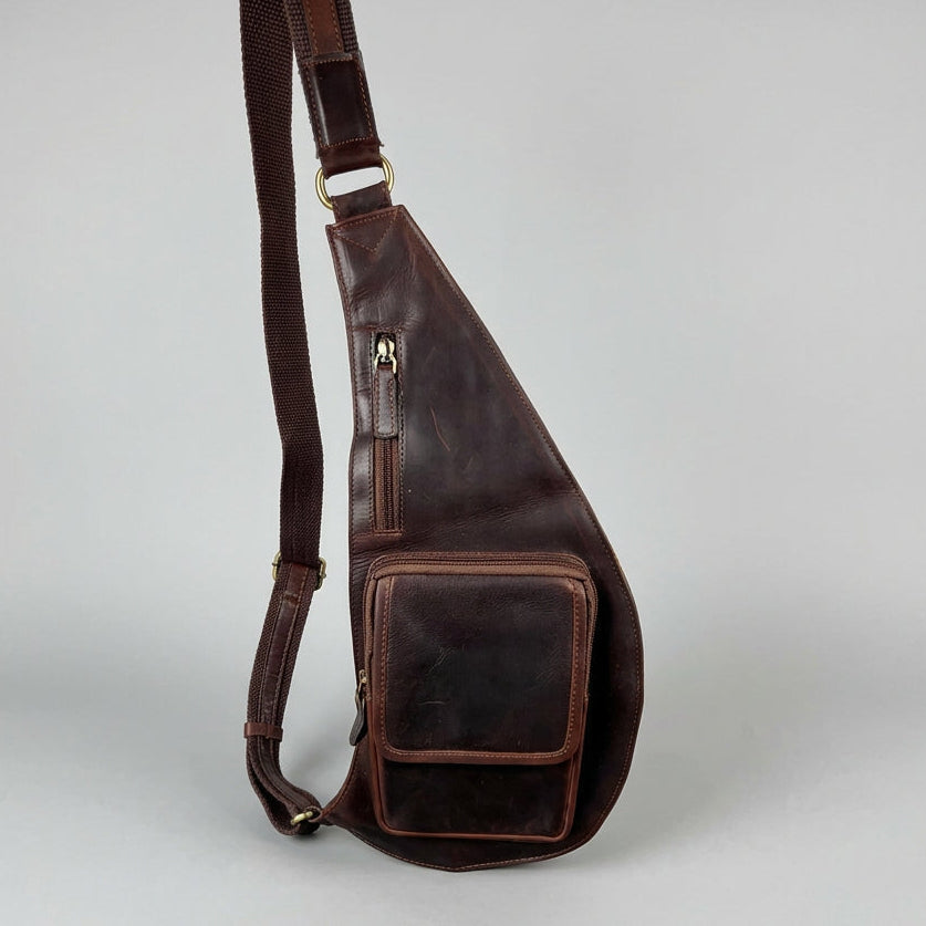 A dark brown leather sling bag with a wide adjustable shoulder strap