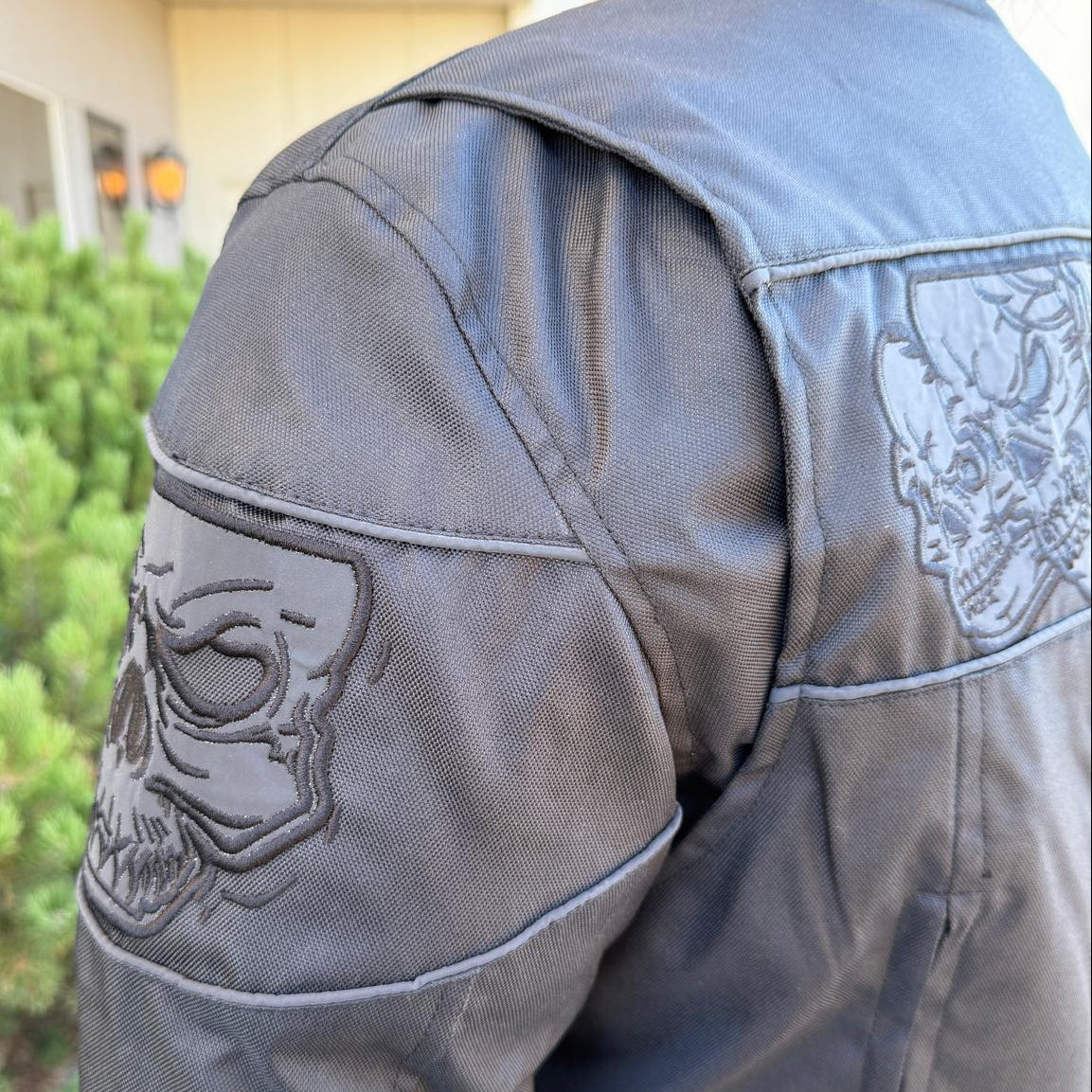 A man wearing a black bomber motorcycle jacket with intricate black embroidery across the chest
