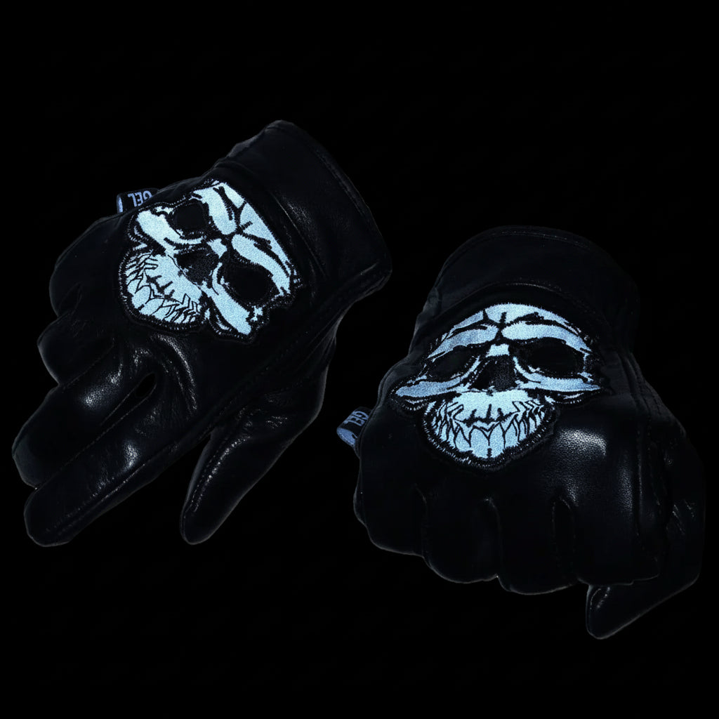 Black gloves with skull design on a dark background, featuring Gel Palm reflective material branding.