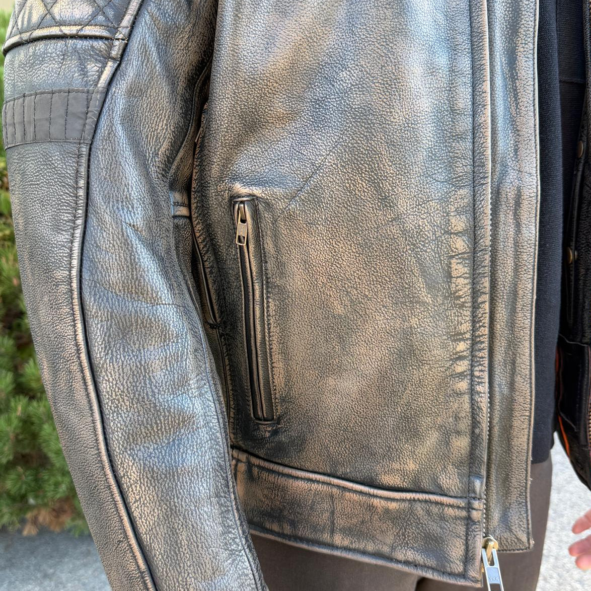 A man wearing a distressed brown leather motorcycle jacket with geometric diamond-stitch detailing on the shoulders