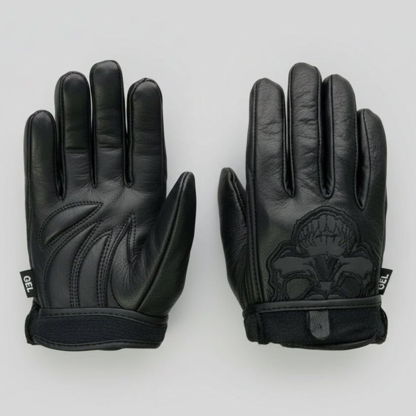 A pair of black leather motocross gloves shown from both front and back views on a white background with graphic overlays. The left glove shows the back of the hand with textured panels, while the right glove shows the palm side with a black skull graphic.