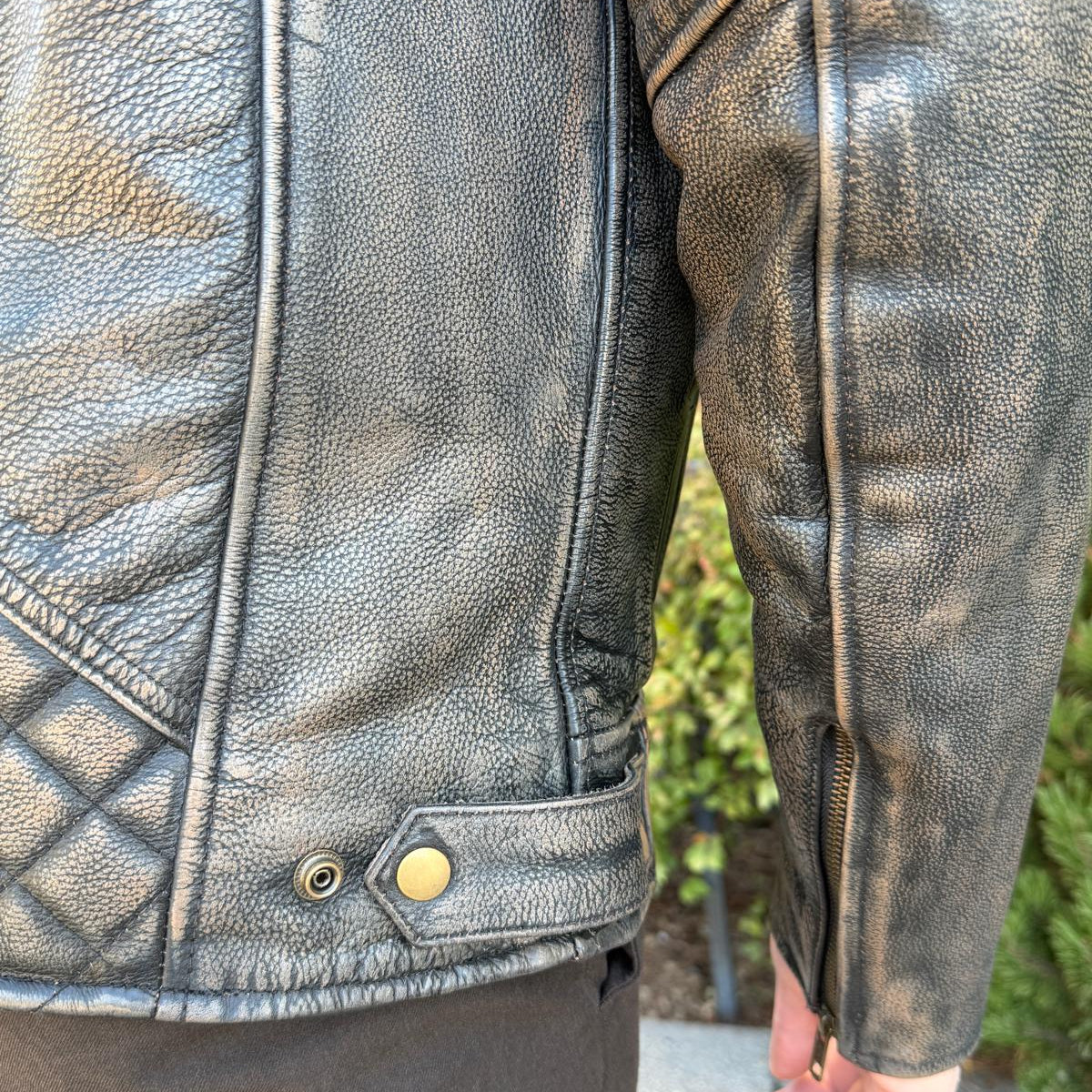 A man wearing a distressed brown leather motorcycle jacket with geometric diamond-stitch detailing on the shoulders
