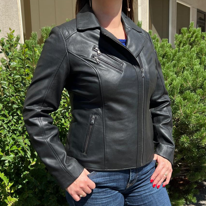 Woman wearing a black leather jacket and blue jeans standing outdoors.