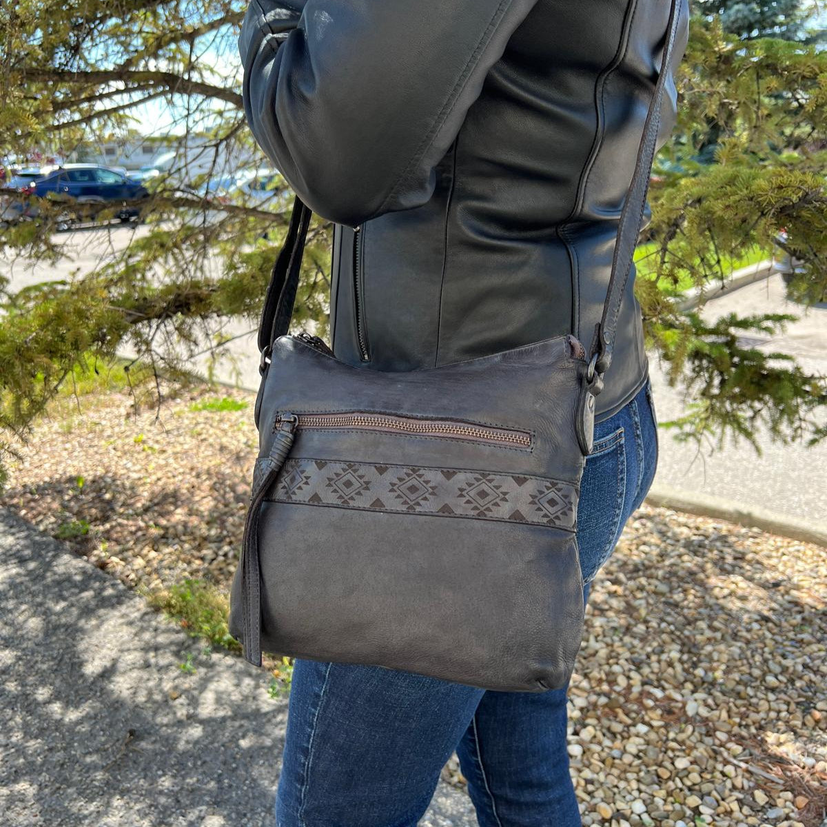 Person wearing a gray jacket and carrying a matching gray crossbody bag outdoors.