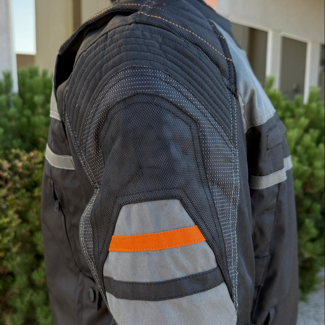 A man wearing a black and gray motorcycle jacket with reflective gray stripes