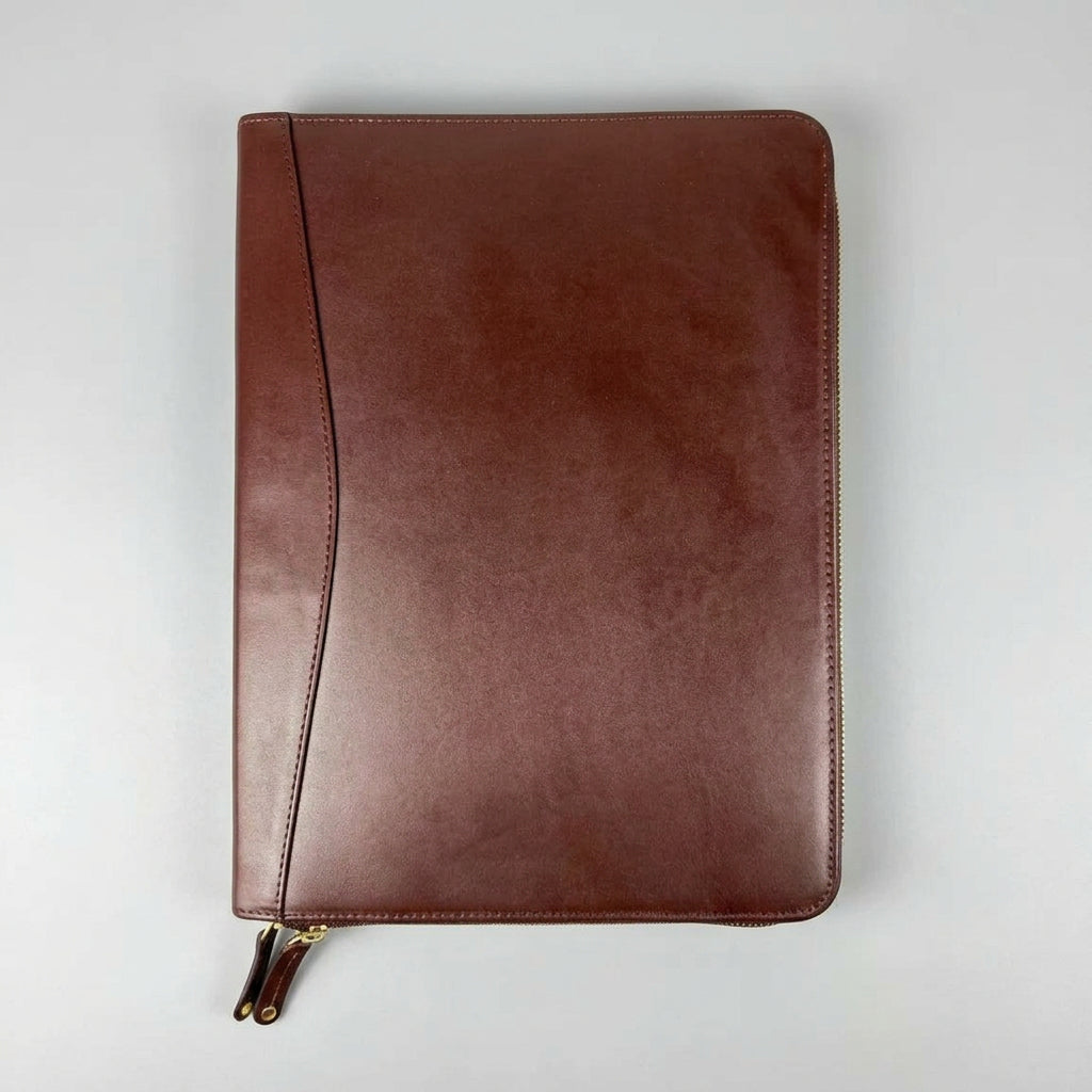 A brown leather zip-around notebook cover with a diagonal stitched detail and a small gold zipper pull