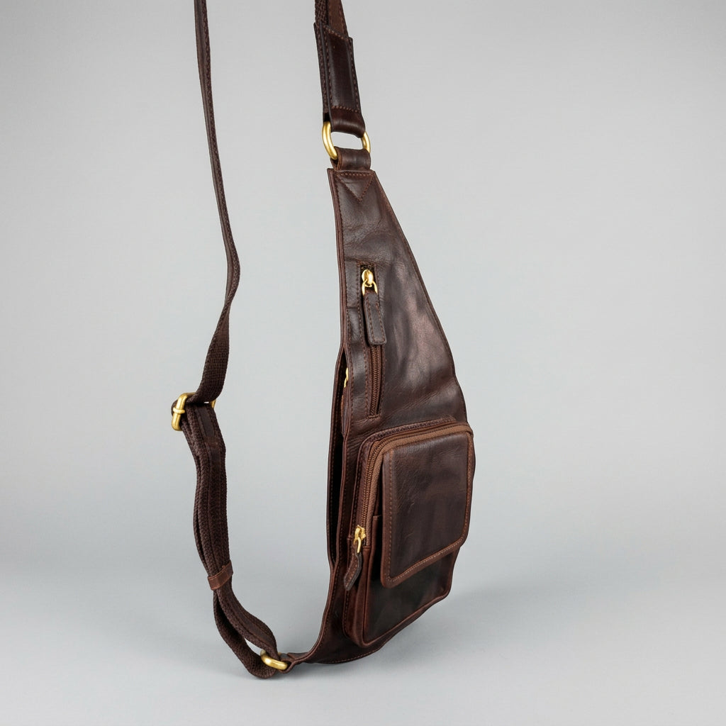 A dark brown leather sling bag with a long shoulder strap and front zippered pocket